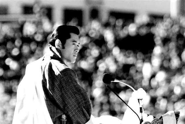 A man in traditional clothing speaks into a microphone before a large crowd.